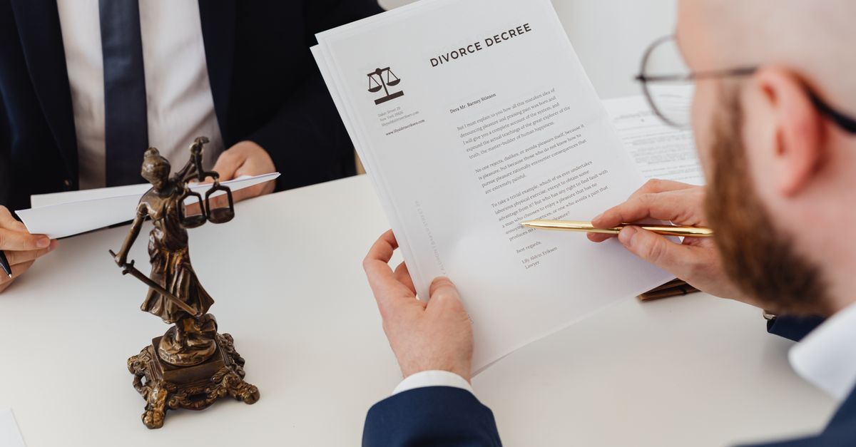 Two professionals examining a divorce decree with a Lady Justice statue nearby.